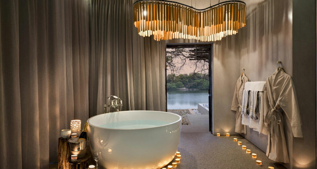 bathroom with a round bath and candles and a hanging chandelier at Matetsi Victoria Falls